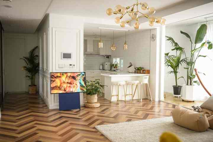 ホワイトとゴールドをアクセントにしたキッチンとキッチンアイランド、大きな植物とスタイリッシュなラグが調和した温かみのある空間