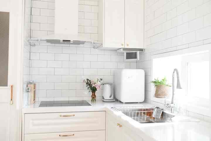 White-toned kitchen featuring white cabinets, hood, and stainless steel sink, presenting a clean and minimal atmosphere