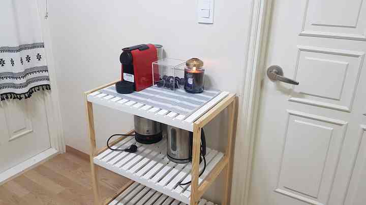 White and natural wood-tone kitchen space featuring a Nespresso capsule coffee machine and lit candle on a tidy shelving unit