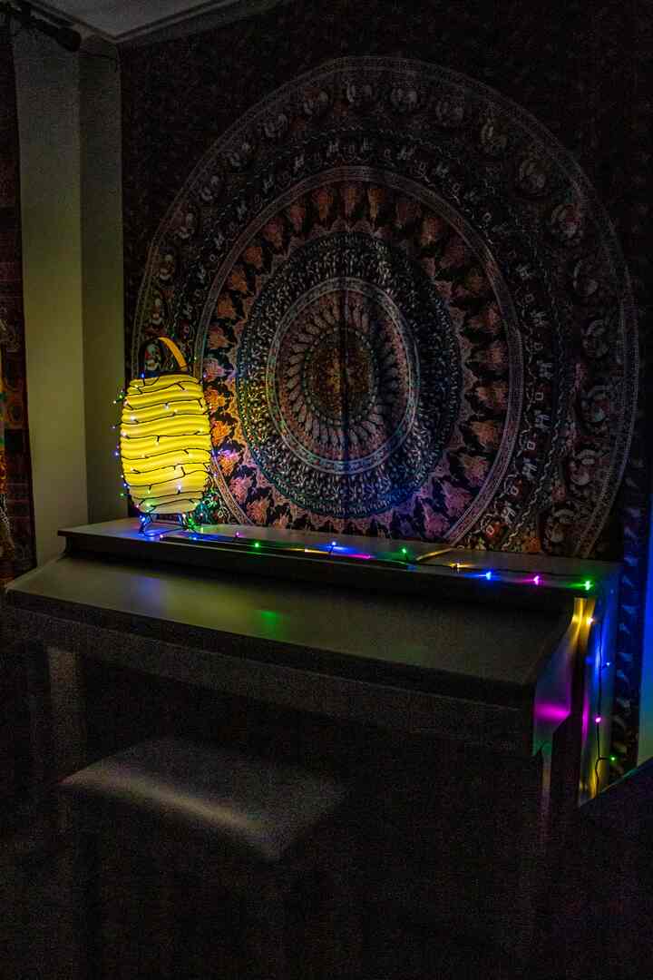 Bohemian style dark room featuring a large patterned wall decor, yellow lamp on table, and colorful string lights