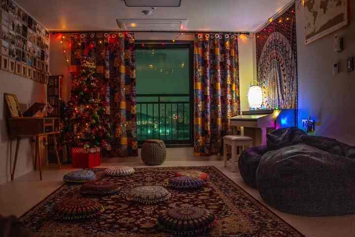 Bohemian style studio living room featuring patterned curtains, large rug, bean bags, and a decorated Christmas tree creating a cozy atmosphere