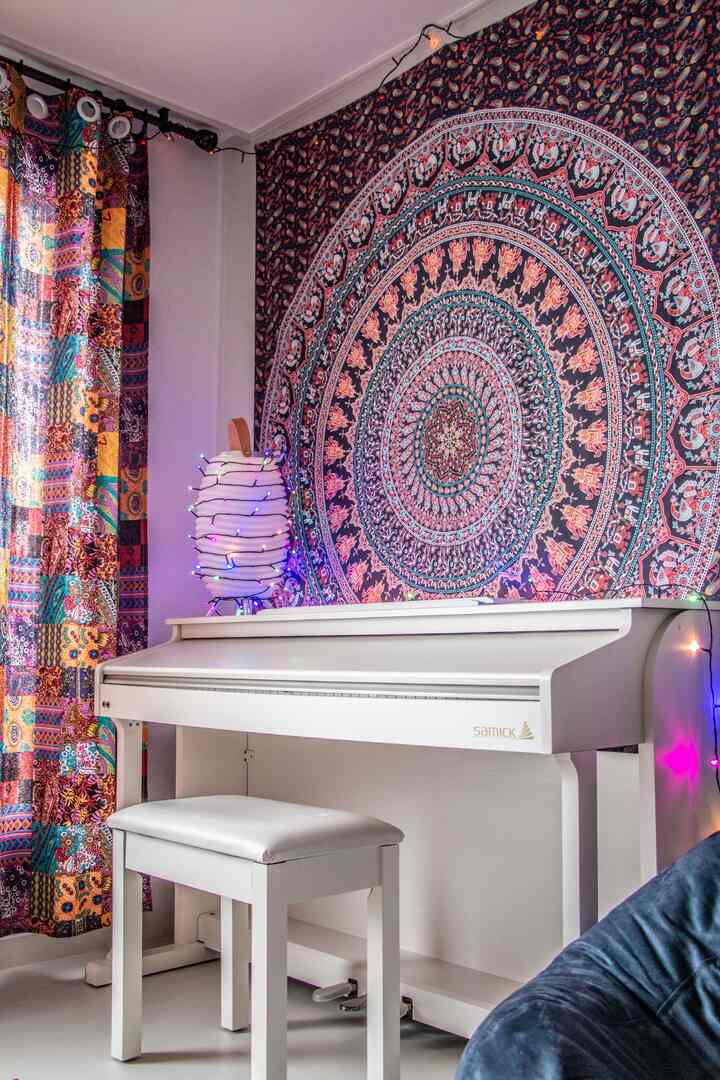ボヘミアン柄のマンダラタペストリーと白いピアノが配置された印象的な室内、クリスマスのストリングライトが温かい雰囲気を演出
