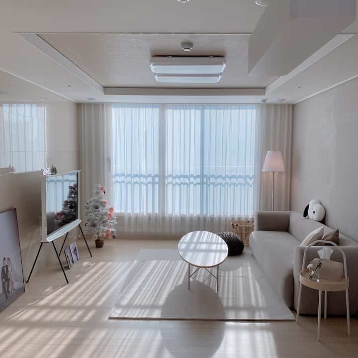 White and beige toned living room featuring a sofa, rug, and curtains with a clean and warm atmosphere
