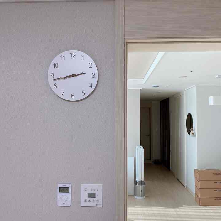 A clean and natural living space in soft beige and white tones, featuring a simple wall clock hung on the central wall