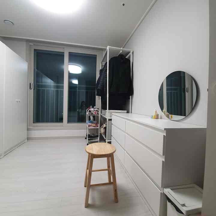 ホワイトとナチュラルカラーのウォークインクローゼット、シンプルなハンガーラックとチェスト、木製スツールが配置された清潔感のあるインテリア