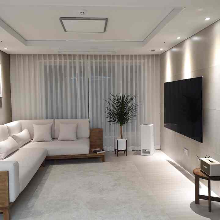 A white and beige toned living room featuring modern natural sofa, large TV, and bright sheer curtains creating a serene atmosphere