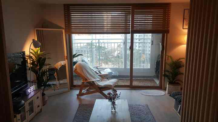 暖かみのあるウッドトーンとベージュのリビング、木製のアームチェアとコーヒーテーブル、フロアランプや植物が配置された落ち着いた空間