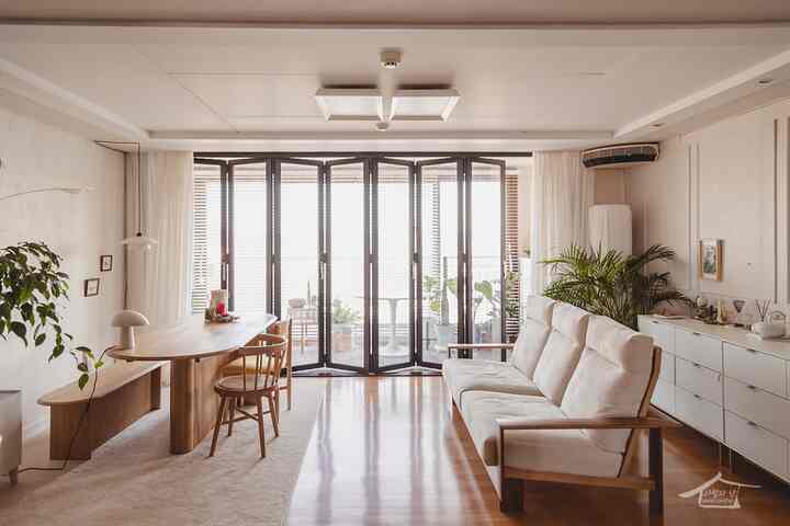 Natural wood tone and white living room featuring folding doors, sofa, and dining table with warm atmosphere