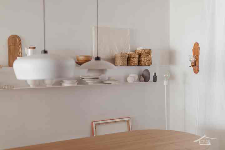 White and natural toned kitchen space featuring neatly arranged tableware and wooden items on a shelf with a simple interior