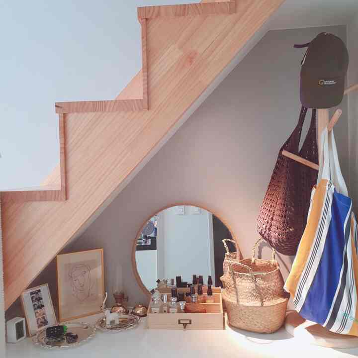 Natural wood tone entrance under staircase featuring wooden cosmetic organizer, rattan baskets, coat rack, and round mirror in a cozy arrangement