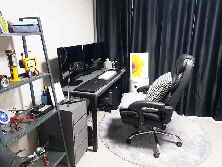 Monotone computer room featuring a black desk, office chair, blackout curtains, and a round rug, creating a functional space