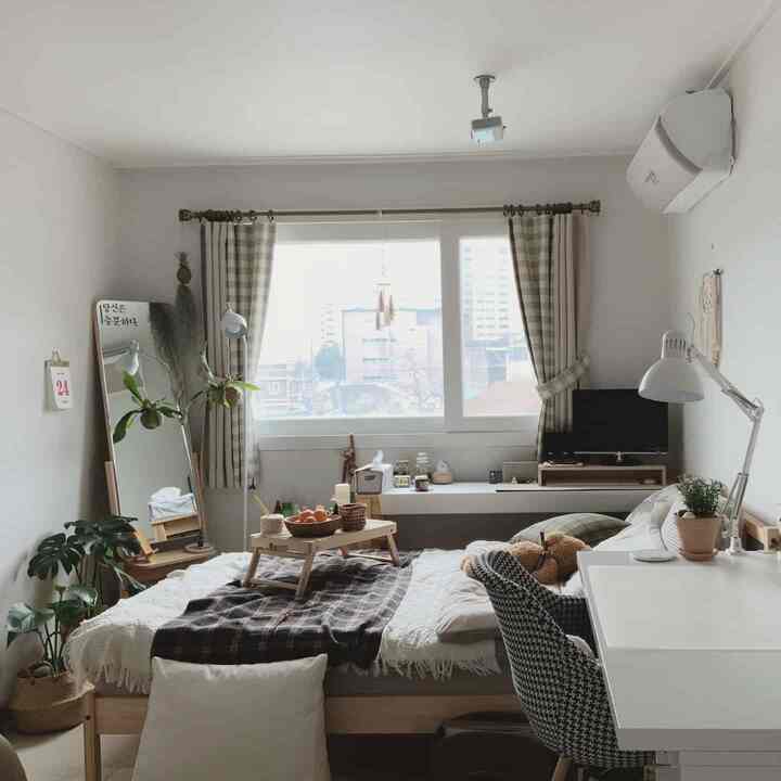 Bright white and wood-tone bedroom with checkered curtains and plants by the window, featuring a cozy home office setup
