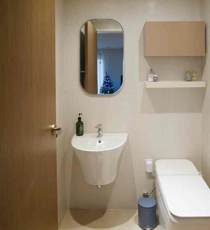 A small, neat first-floor guest restroom in white and brown tones featuring sink, toilet, wall-storage cabinet, and mirror in a clean space