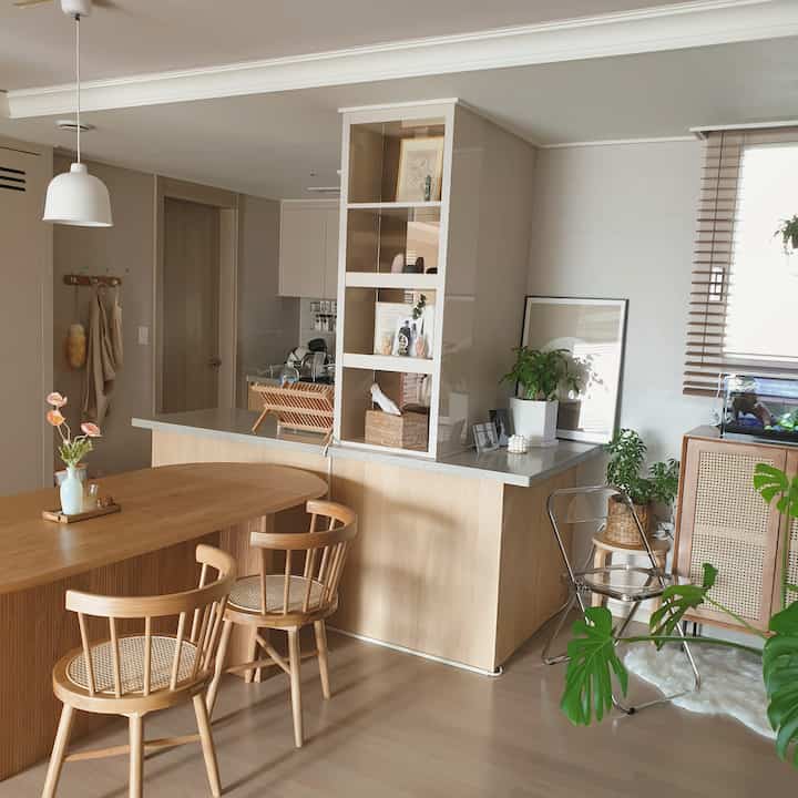 ナチュラルな木目調とベージュ色の2人暮らし向けキッチン兼ダイニングスペース。ラタンチェアや植物で温かみのある雰囲気のインテリア