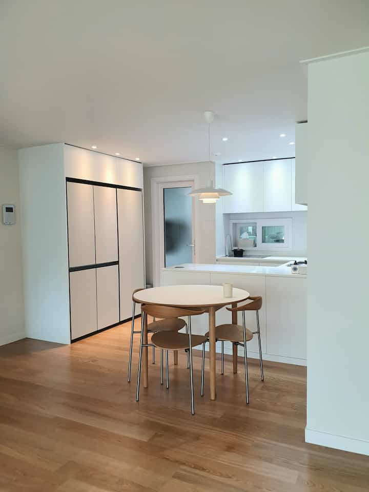 Modern dining room in white and wood tones featuring a round dining table and clean kitchen setup