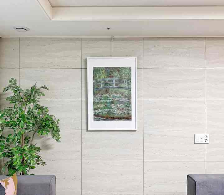 Beige tiled wall featuring a Claude Monet framed poster and a plant on the left in a modern living room interior