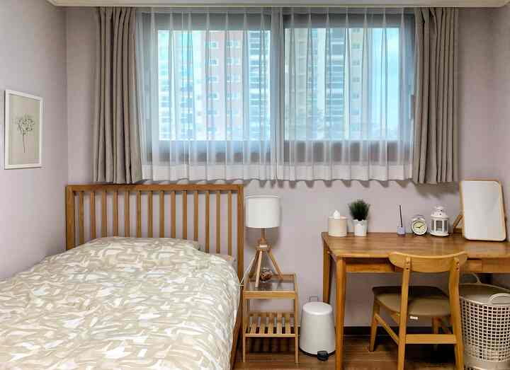 Light purple-walled small bedroom featuring natural wood furniture with bed and workspace arranged for cozy living