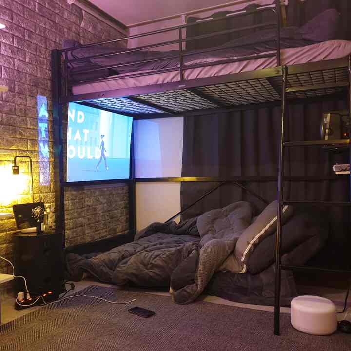 Black-toned compact bedroom featuring a loft bed with mattress below and a large screen creating a cozy atmosphere