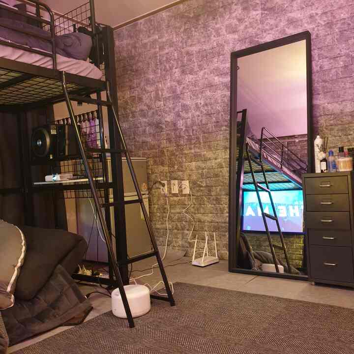Gray brick-patterned wall with black metal furniture, loft bed and full-length mirror in a minimal, modern small bedroom