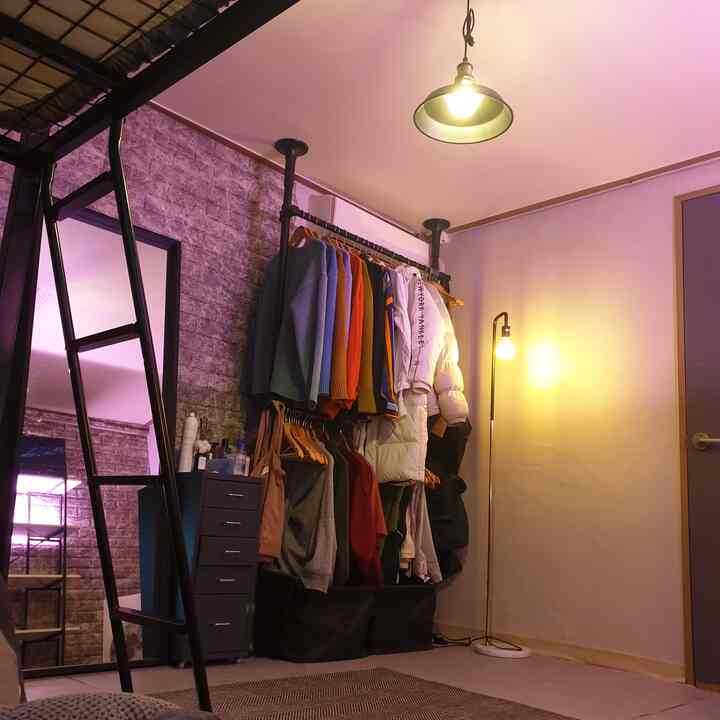 ダークグレーのトーンの寝室、メタルのハンガーラックとドレッサー、ペンダントライトとフロアランプが配置されたモダンでインダストリアルな空間