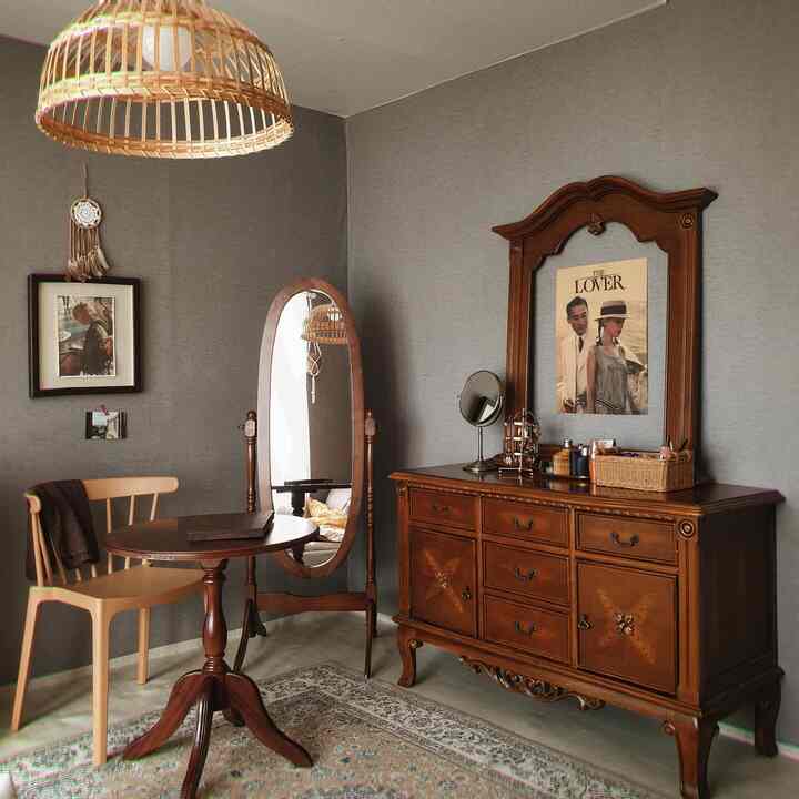 Gray-walled vintage bedroom corner featuring wood-tone antique furniture and woven pendant light