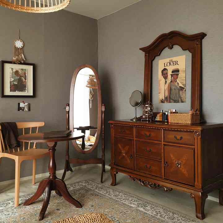 グレーの壁と木目調のアンティーク化粧台、鏡、丸テーブルが配置された雰囲気のある寝室