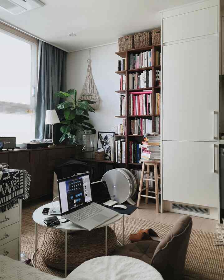 Natural-toned living room featuring a bookshelf and round table with laptop for remote working, creating cozy atmosphere