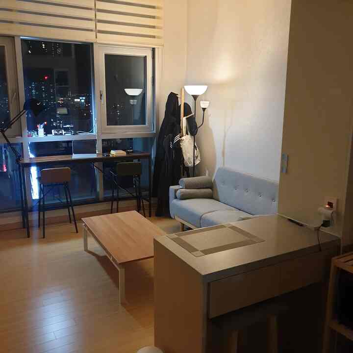 White and natural brown tone studio living space with gray sofa, wooden table, bar stools, and a home office area