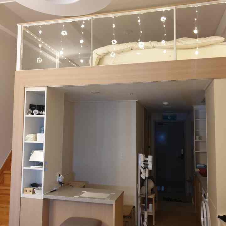 White and wood-tone loft studio apartment featuring kitchen island, stool, loft bedroom, and pendant lights creating a cozy interior