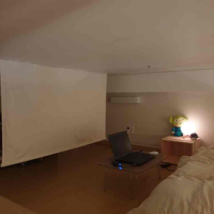 Warm brown and beige toned small bedroom featuring a wooden bedside table and a large white projection screen for home cinema