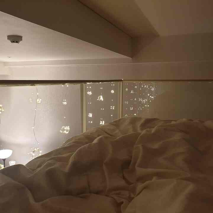 暖かいベージュの寝具が置かれた寝室、窓に沿って柔らかく光るストリングライトが印象的な雰囲気のあるインテリア