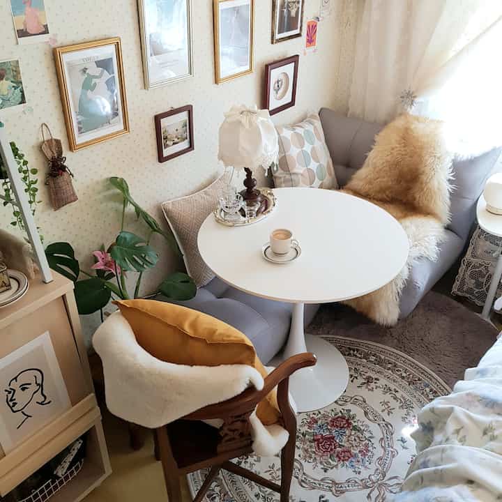 Natural toned studio apartment home cafe featuring a gray sofa, white round dining table, cushions, and a cozy rug
