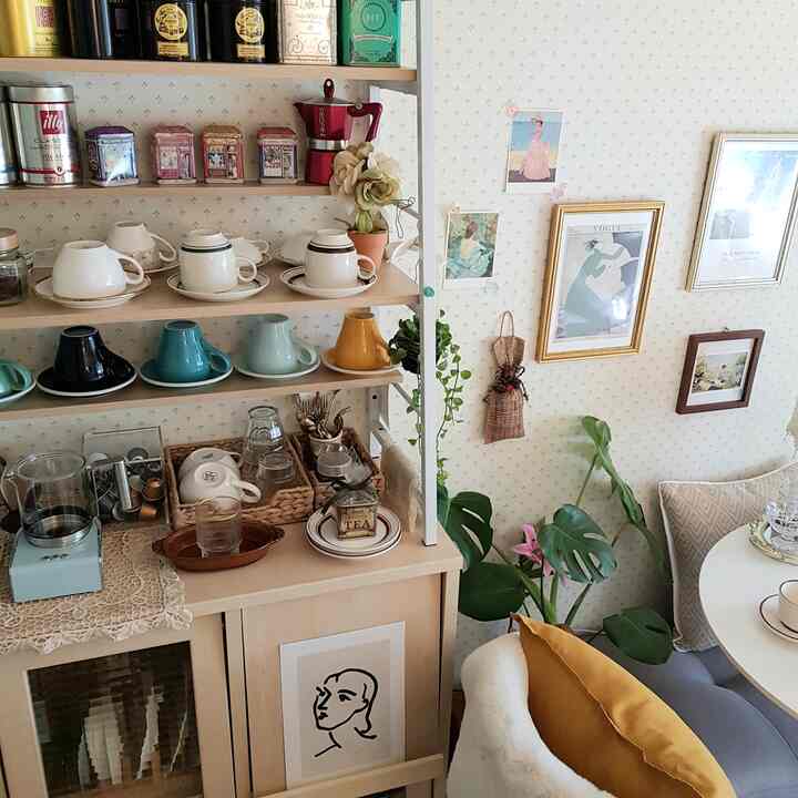 やわらかなナチュラルトーンのホームカフェ空間、木製の棚にカラフルなコーヒーカップと壁に掛けられた額装アートが温かみのある雰囲気を醸し出すインテリア