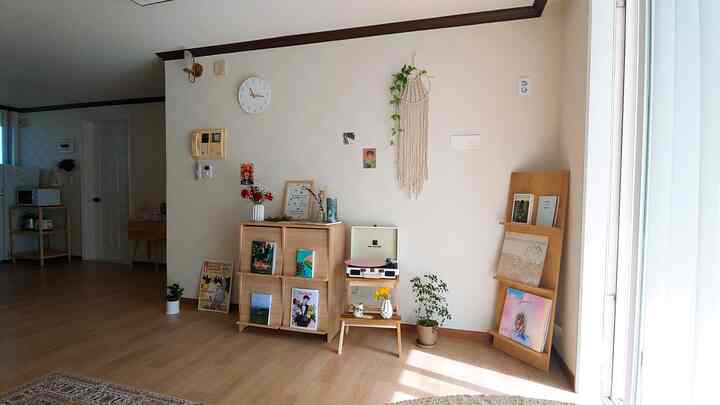 Natural wood tone living room featuring wooden stand bookshelf, wall clock, LP turntable, and macramé creating cozy atmosphere