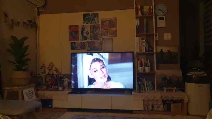 White and brown toned living room featuring TV stand, bookshelf, and posters in a cozy compact space