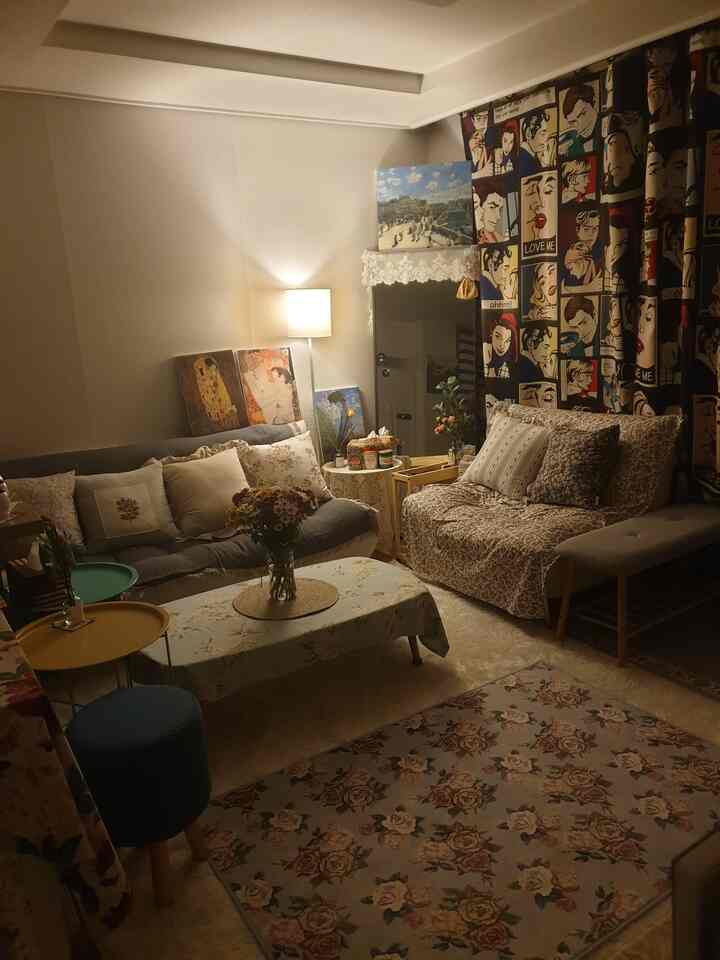 Cozy living room with warm lighting, floral patterned sofas, and pop art blackout curtains