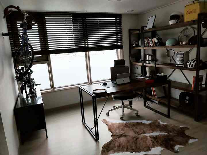 A modern studio home office in black and light brown tones featuring a desk, office chair, bicycle, and storage bookshelf