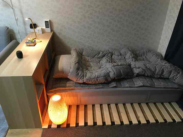 Natural toned studio bedroom featuring wood bed frame and checkered bedding in a simple interior