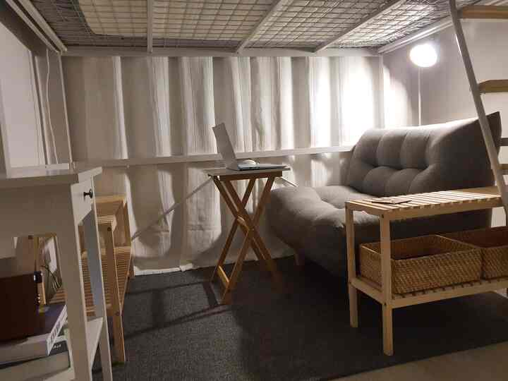 白い壁とカーテン、木目調家具とグレーのソファが配置された狭くコンパクトな二段ベッド休憩スペース