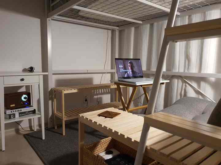 Small bedroom with white and natural wood tones, featuring a bunk bed, compact desk with laptop, and shelving, creating a cozy atmosphere