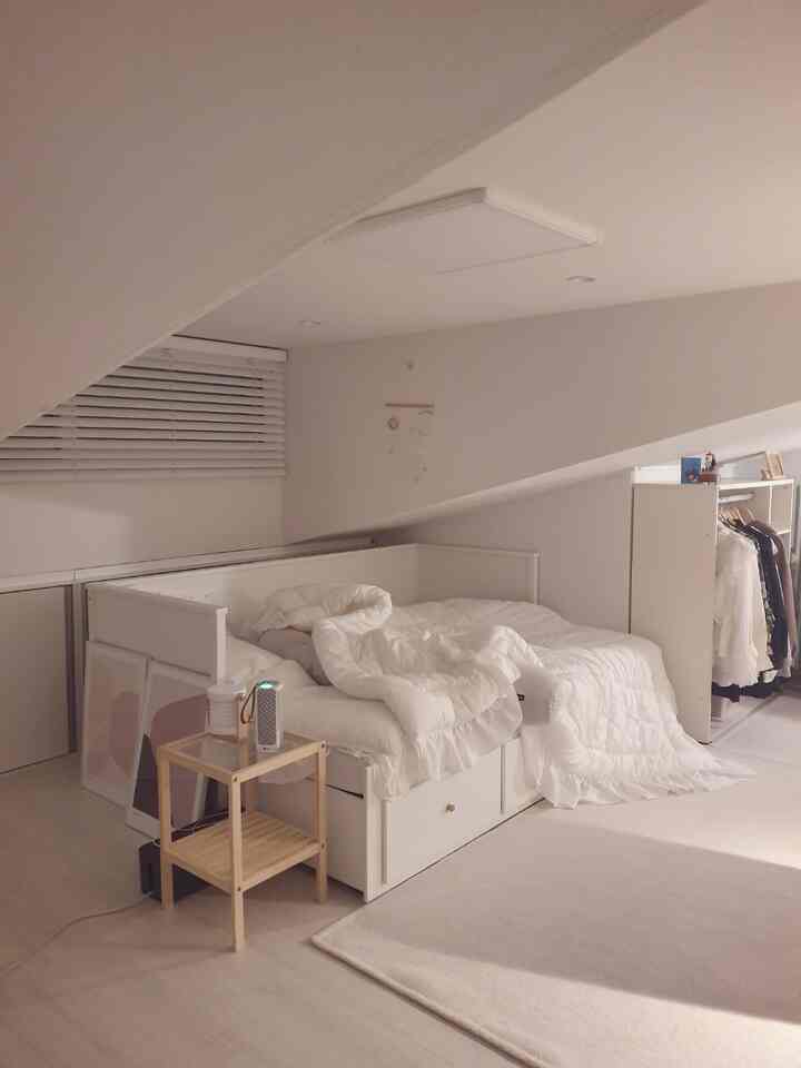 明るい白色調のロフト、中央にベッドと木製サイドテーブルが配置された落ち着いた空間