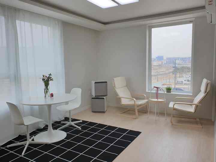 Bright white and wood-tone small cozy home cafe space featuring round table and armchairs by large window, creating a calm atmosphere