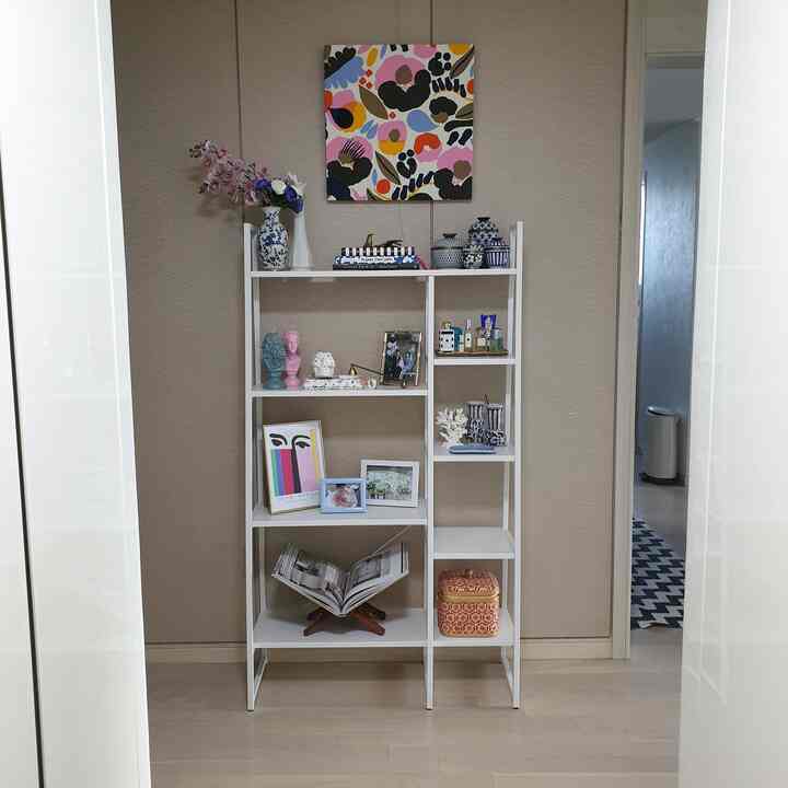 Natural toned entrance with beige walls and light wood flooring, featuring a white metal shelf adorned with various picture frames and decor creating cozy atmosphere
