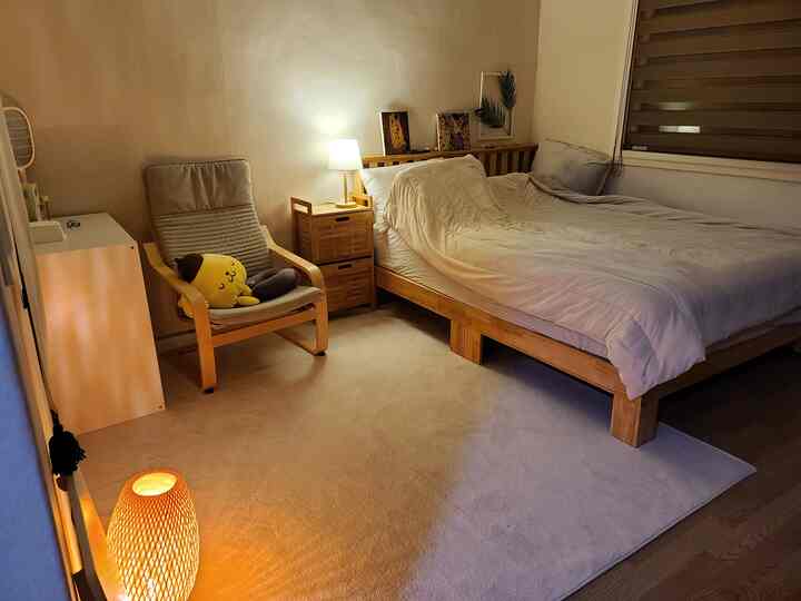 暖かいベージュと木目調の寝室、木製ベッドとアームチェア、ラグが落ち着いた雰囲気を作るインテリア