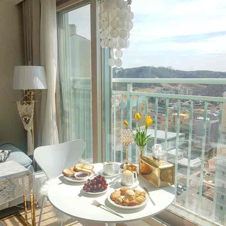 Bright white and yellow-toned living space with balcony, featuring a round table with coffee cups and a shell mobile creating cozy ambiance