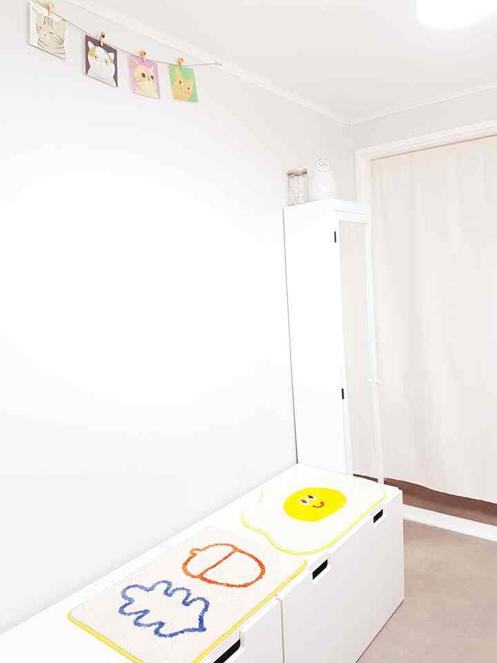 Bright white-toned kids' room featuring a tall mirror cabinet and storage bench topped with cute rugs in a simple storage space