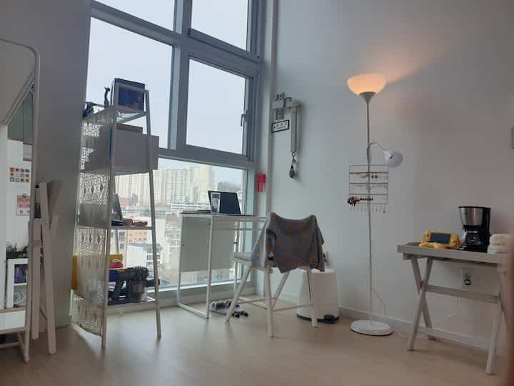 Natural tone studio loft featuring white furniture, folding chair, shelves, and compact desk with a cozy home office vibe