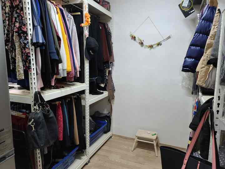 Compact white-walled dressing room with wood-tone flooring, featuring clothes racks on both sides and a central stool, designed for practical storage