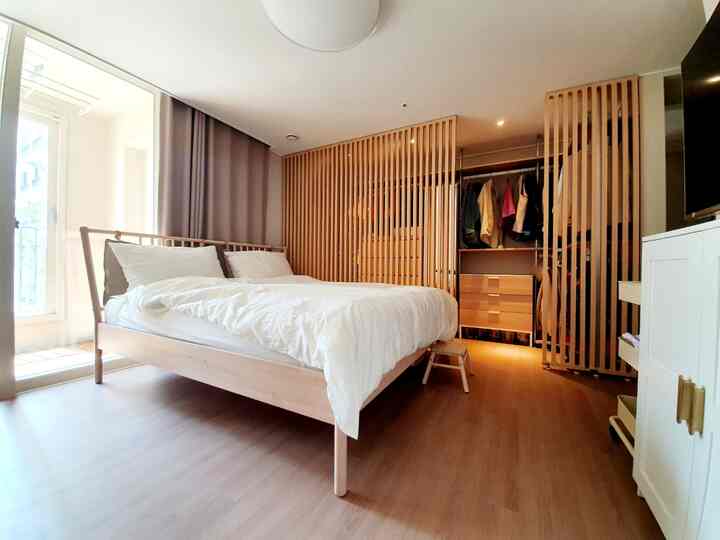 Bright white and wood-tone bedroom featuring a large bed and walk-in closet separated by wooden slat partition, creating a cozy atmosphere