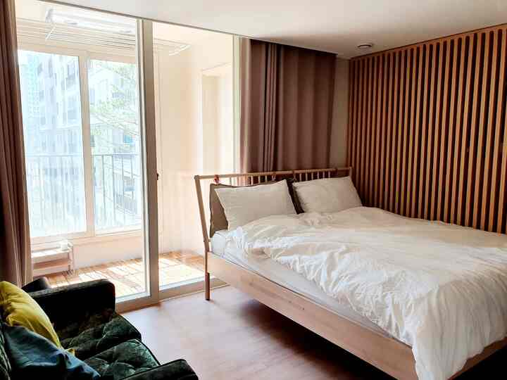 Natural modern bedroom featuring white bedding, wood tones, curtains, and a sunlit veranda space